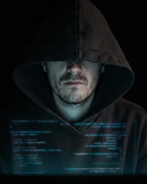 Julio im dunklen Hoodie, nur vom Bildschirm beleuchtet, Kapuze tief über den Augen. KI-bearbeitetes Foto.