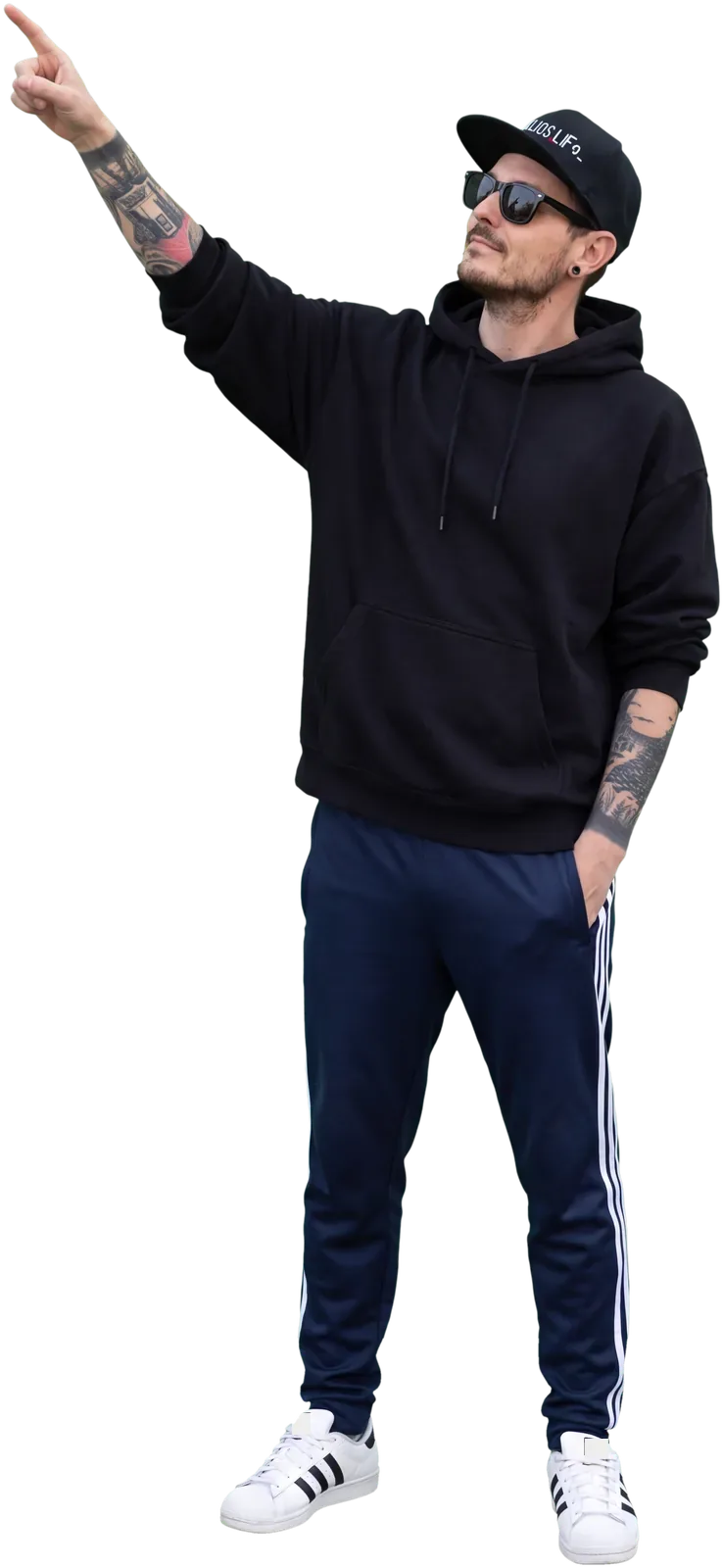Julio steht an der Wand und zeigt nach oben aufs Etikett: schwarze Cap mit julios.life-Schriftzug, schwarzer Hoodie, dunkelblaue Trainingshose, weiße Sneaker. KI-generiertes Bild nach Fotos von Julio.